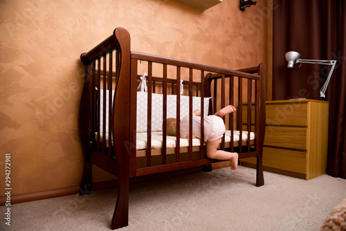 Foto the child is trying to get into the crib through the hole that was formed due to the missing part