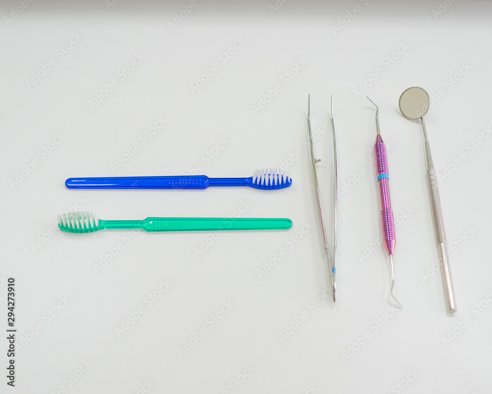 Dentist's table with sterile tools on a white background top view. A mirror, tweezers, a probe and a toothbrush are on the doctor table. Oral hygiene, caries prevention, examination. Dentist's table with sterile tools on a white background top view. A mirror, tweezers, a probe and a toothbrush are on the doctor table. Oral hygiene, caries prevention, examination.