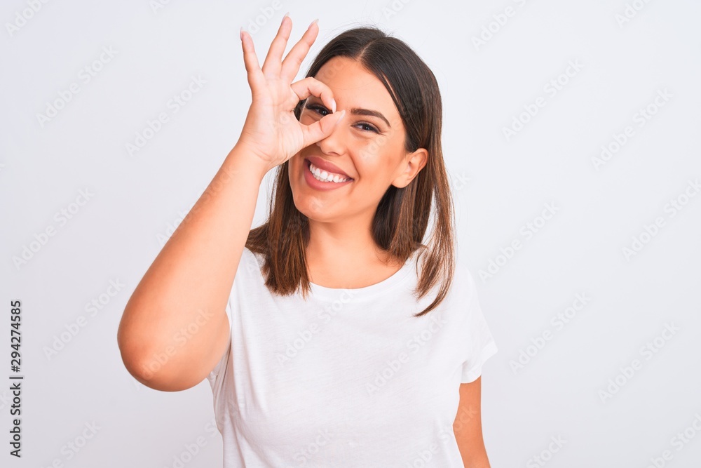 Portrait of beautiful and young brunette woman standing over isolated white background doing ok gesture with hand smiling, eye looking through fingers with happy face. Portrait of beautiful and young brunette woman standing over isolated white background doing ok gesture with hand smiling, eye looking through fingers with happy face.