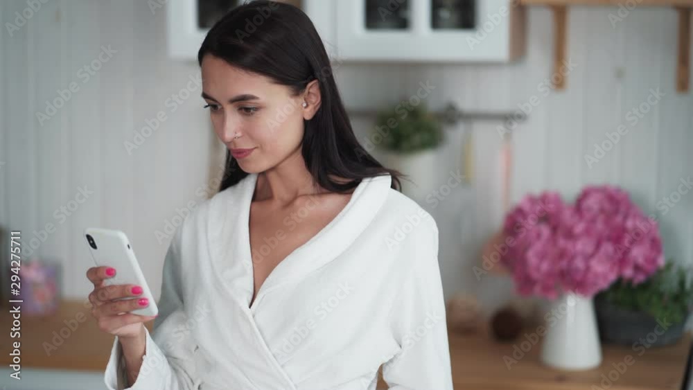 Woman in white bathrobe sends message on mobile, uses phone for work from home Woman in white bathrobe sends message on mobile, uses phone for work from home