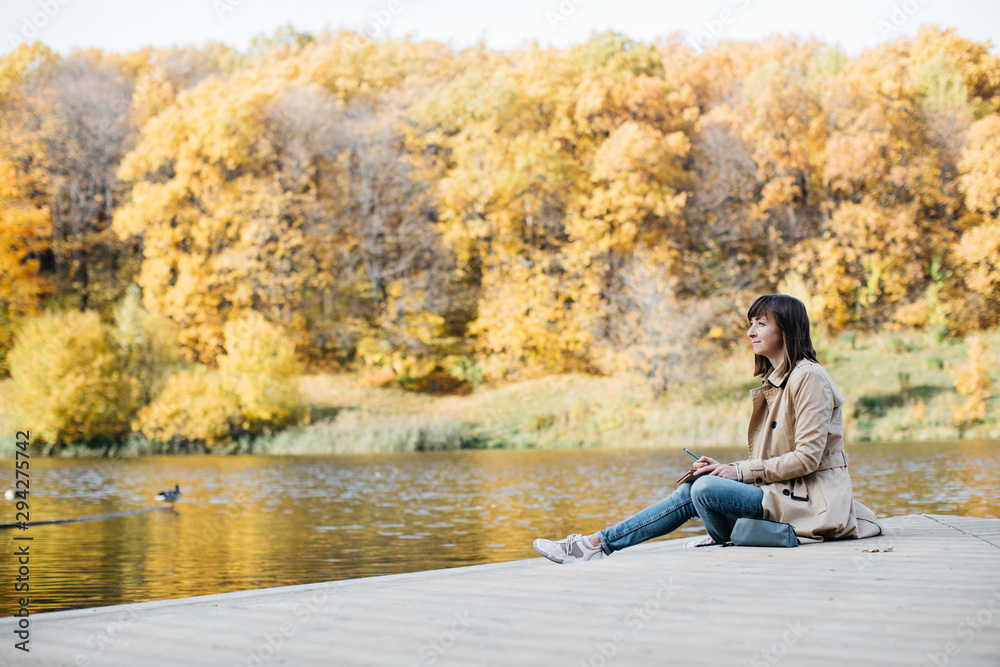 A young girl sketching near a lake in the autumn forest.