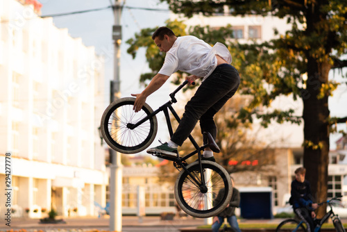 The guy performs a stunt on BMX, jumping up, and touches the front wheel.
