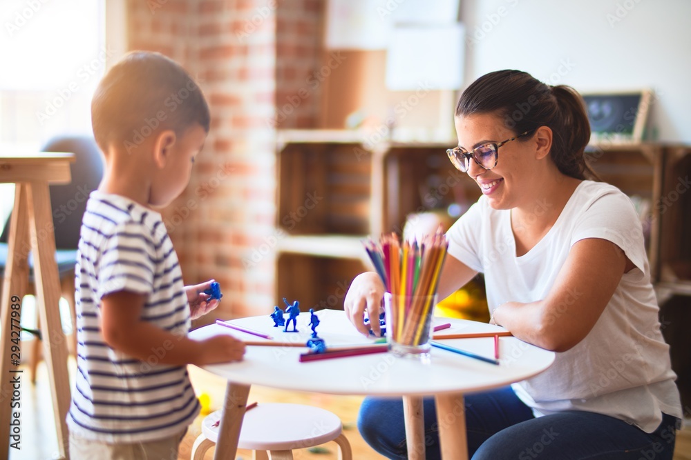 Beautiful teacher and toddler boy playing with figurine army soldiers at kindergarten Beautiful teacher and toddler boy playing with figurine army soldiers at kindergarten
