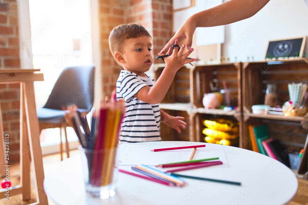 Beautiful teacher and toddler boy drawing draw using colored pencils at kindergarten Beautiful teacher and toddler boy drawing draw using colored pencils at kindergarten