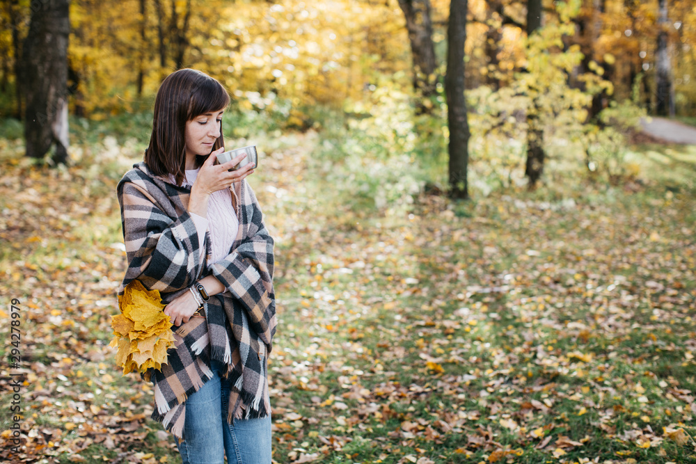 Girl in the autumn forest drinking tea with leaves in his hands. The girl is in a great mood and happy Girl in the autumn forest drinking tea with leaves in his hands. The girl is in a great mood and happy