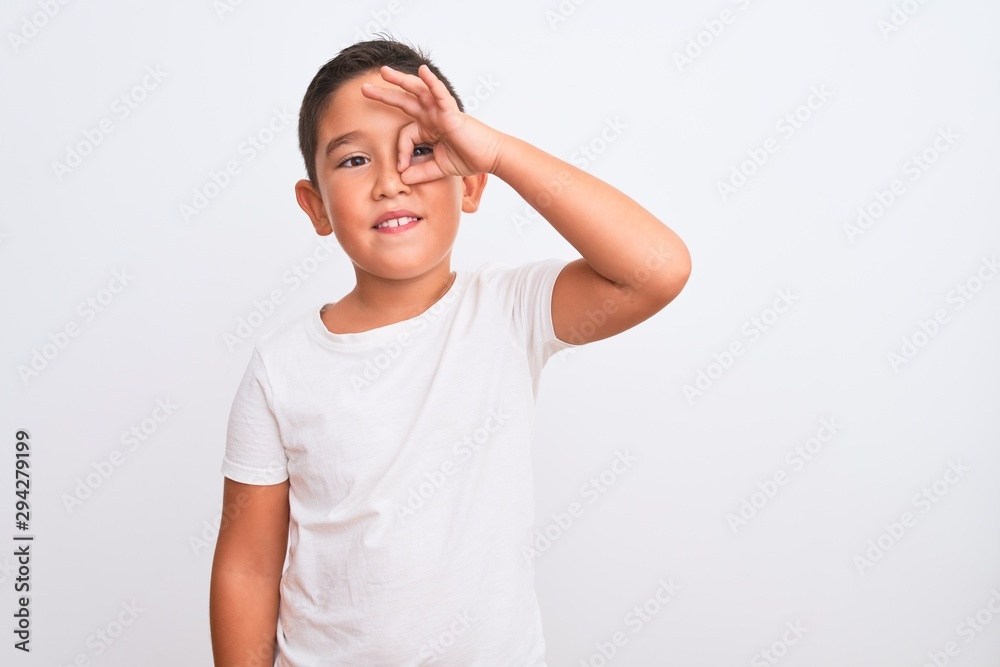 Beautiful kid boy wearing casual t-shirt standing over isolated white background doing ok gesture with hand smiling, eye looking through fingers with happy face. Beautiful kid boy wearing casual t-shirt standing over isolated white background doing ok gesture with hand smiling, eye looking through fingers with happy face.