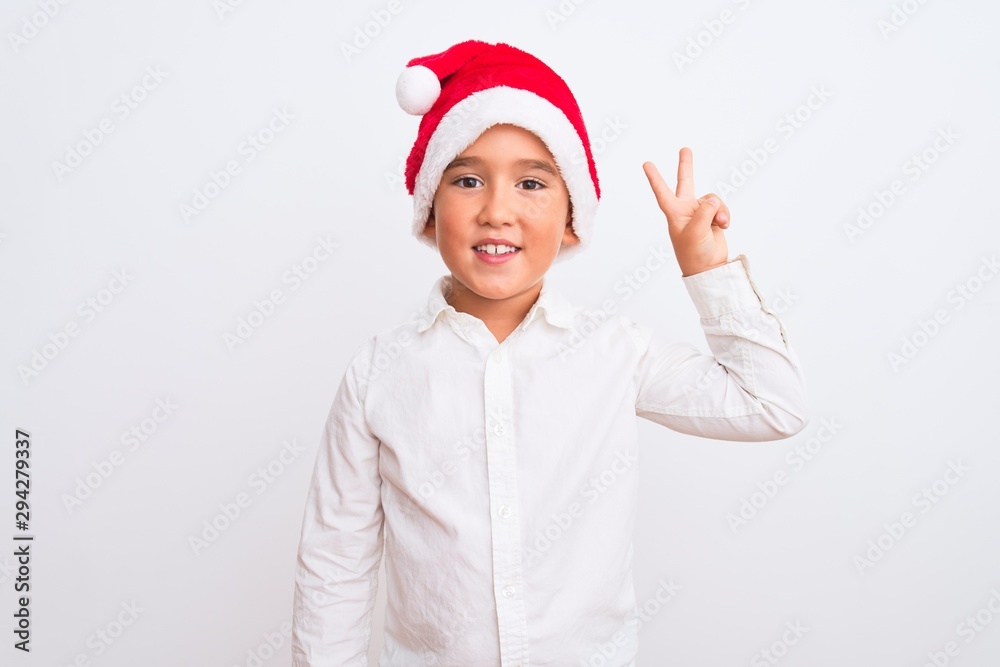 Beautiful kid boy wearing Christmas Santa hat standing over isolated white background showing and pointing up with fingers number two while smiling confident and happy. Beautiful kid boy wearing Christmas Santa hat standing over isolated white background showing and pointing up with fingers number two while smiling confident and happy.