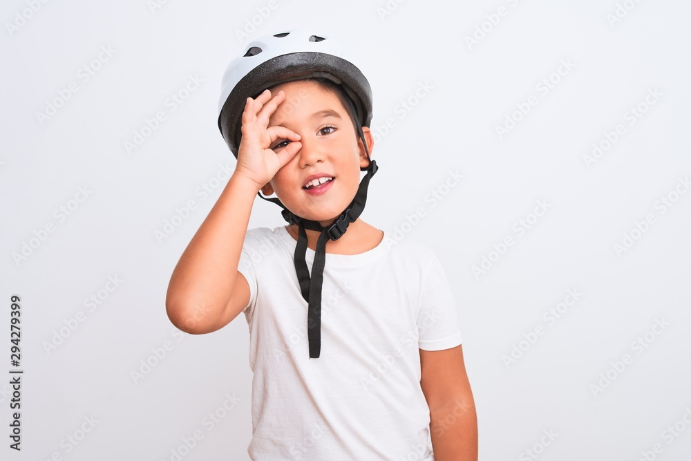 Beautiful kid boy wearing bike security helmet standing over isolated white background doing ok gesture with hand smiling, eye looking through fingers with happy face. Beautiful kid boy wearing bike security helmet standing over isolated white background doing ok gesture with hand smiling, eye looking through fingers with happy face.