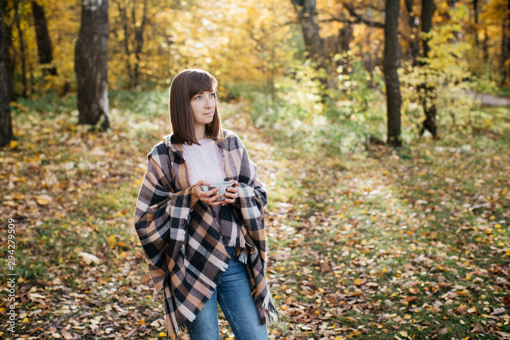 Girl in the autumn forest drinking tea from a thermos. The girl is in a great mood and happy