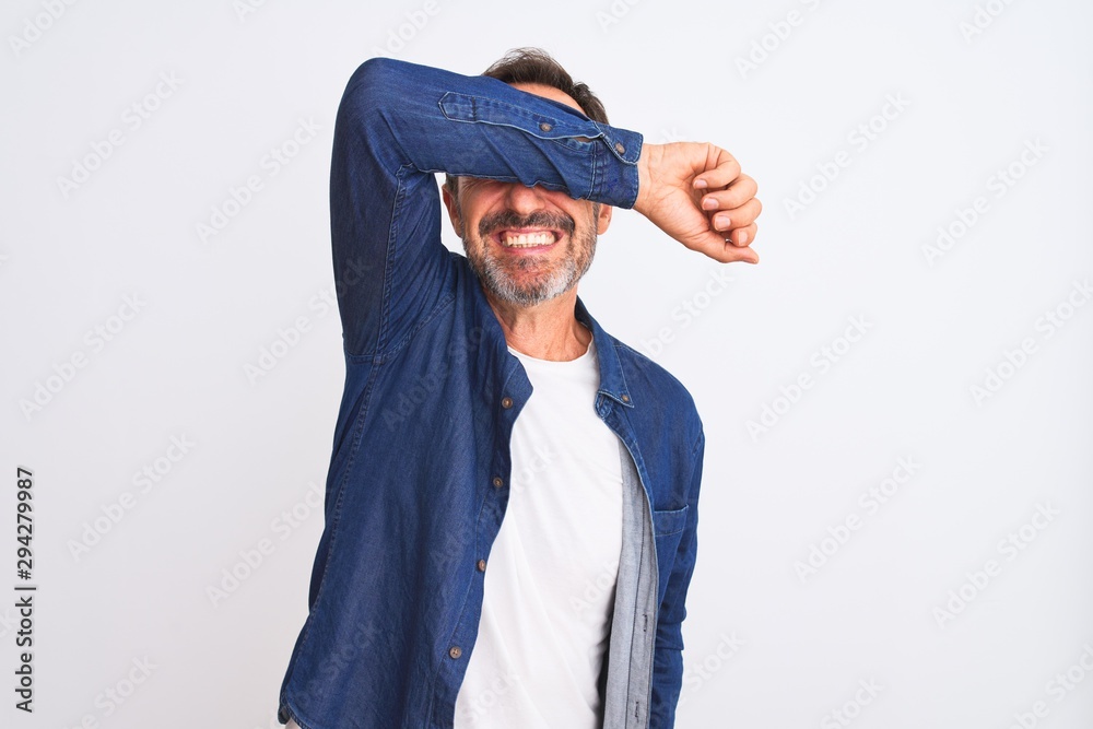 Middle age handsome man wearing blue denim shirt standing over isolated white background covering eyes with arm smiling cheerful and funny. Blind concept. Middle age handsome man wearing blue denim shirt standing over isolated white background covering eyes with arm smiling cheerful and funny. Blind concept.