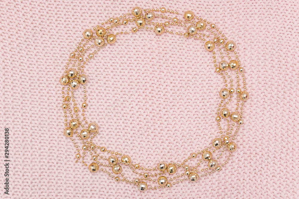 Obraz premium Circle frame from golden beads garland on knitted pink background. Top view Flat lay Template for design