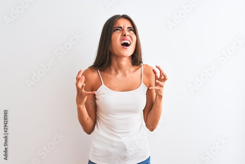 Young beautiful woman wearing casual t-shirt standing over isolated white background crazy and mad shouting and yelling with aggressive expression and arms raised. Frustration concept.