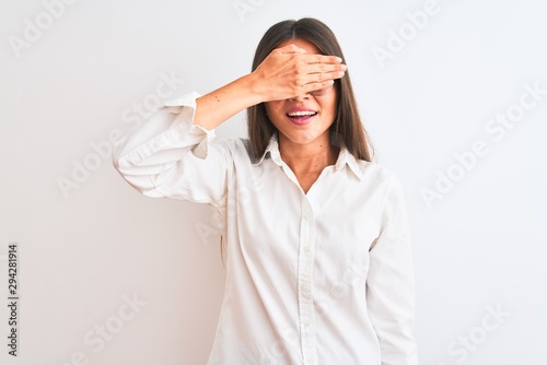 Young beautiful businesswoman wearing glasses standing over isolated white background smiling and laughing with hand on face covering eyes for surprise. Blind concept.