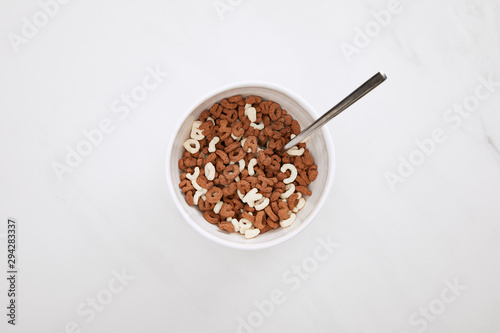 top view of bowl with chocolate and white cereal and spoon on marble surface
