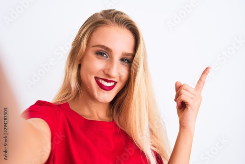 Young beautiful woman wearing t-shirt make selfie by camera over isolated white background very happy pointing with hand and finger to the side