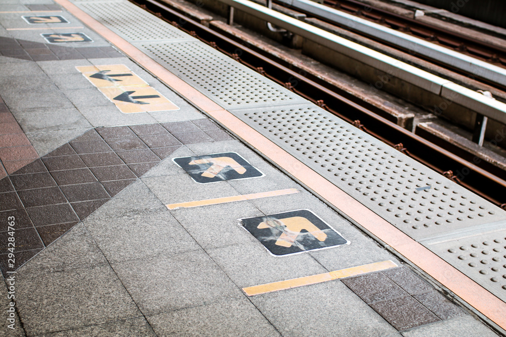 Fototapeta premium Arrow symbol or sign on platform in the queue waiting for the sky train. Yellow arrows on floor platform at sky-train station. Sign for passenger train that is ridden primarily by commuters.