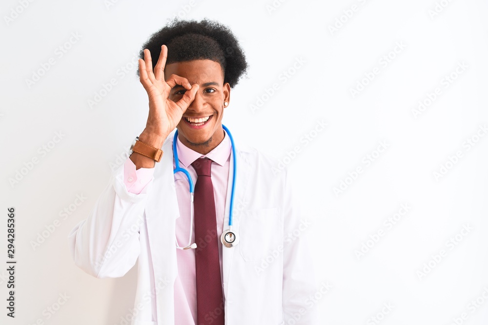 Young african american doctor man wearing sthetoscope over isolated white background doing ok gesture with hand smiling, eye looking through fingers with happy face.