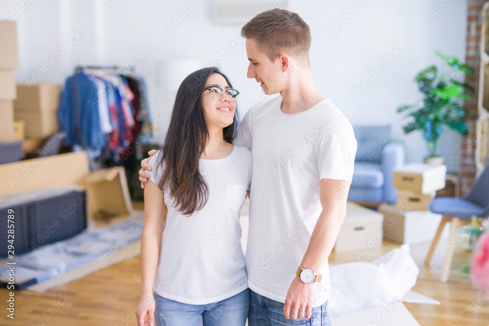 Young beautiful couple standing at new home around cardboard boxes Young beautiful couple standing at new home around cardboard boxes