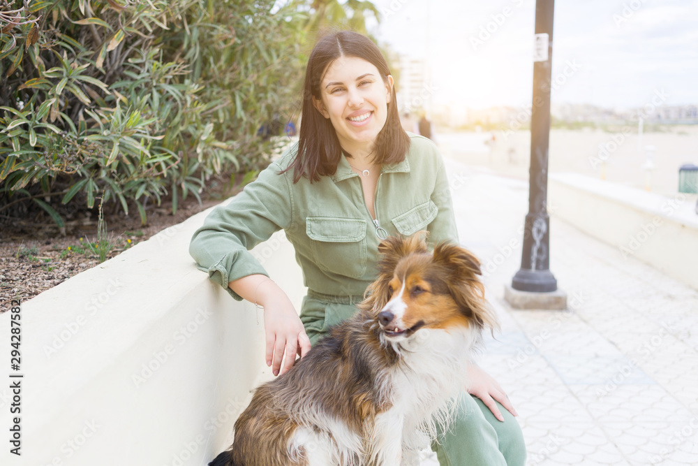 Obraz premium Young beautiful woman sitting on bench in the prominade with her dog