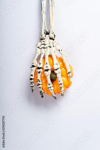Halloween and decoration concept, Skeleton arm catching pumpkin over gray background.