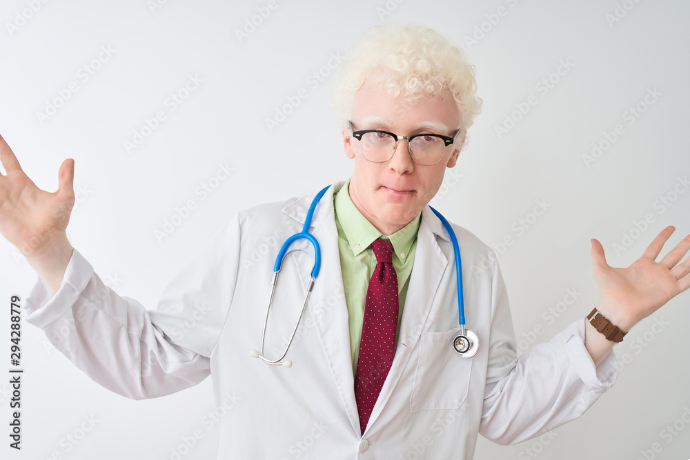 Young albino doctor man wearing stethoscope standing over isolated white background clueless and confused expression with arms and hands raised. Doubt concept. Young albino doctor man wearing stethoscope standing over isolated white background clueless and confused expression with arms and hands raised. Doubt concept.