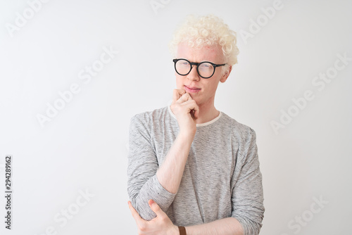 Young albino blond man wearing striped t-shirt and glasses over isolated white background with hand on chin thinking about question, pensive expression. Smiling with thoughtful face. Doubt concept.