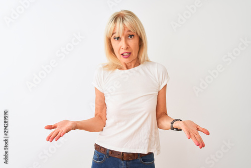 Middle age woman wearing casual t-shirt standing over isolated white background clueless and confused with open arms, no idea concept.