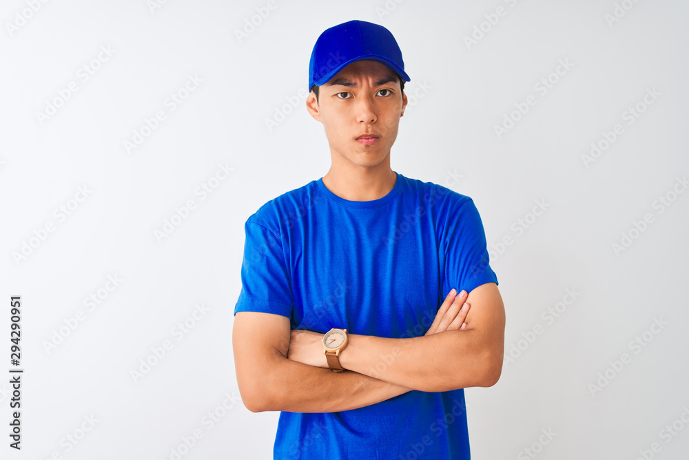 Chinese deliveryman wearing blue t-shirt and cap standing over isolated white background skeptic and nervous, disapproving expression on face with crossed arms. Negative person.