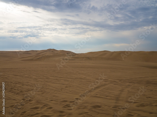 Golden sand dunes at Huacachina desert in Peru, buggies and people in the distance