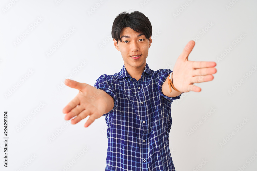 Young chinese man wearing casual blue shirt standing over isolated white background looking at the camera smiling with open arms for hug. Cheerful expression embracing happiness. Young chinese man wearing casual blue shirt standing over isolated white background looking at the camera smiling with open arms for hug. Cheerful expression embracing happiness.