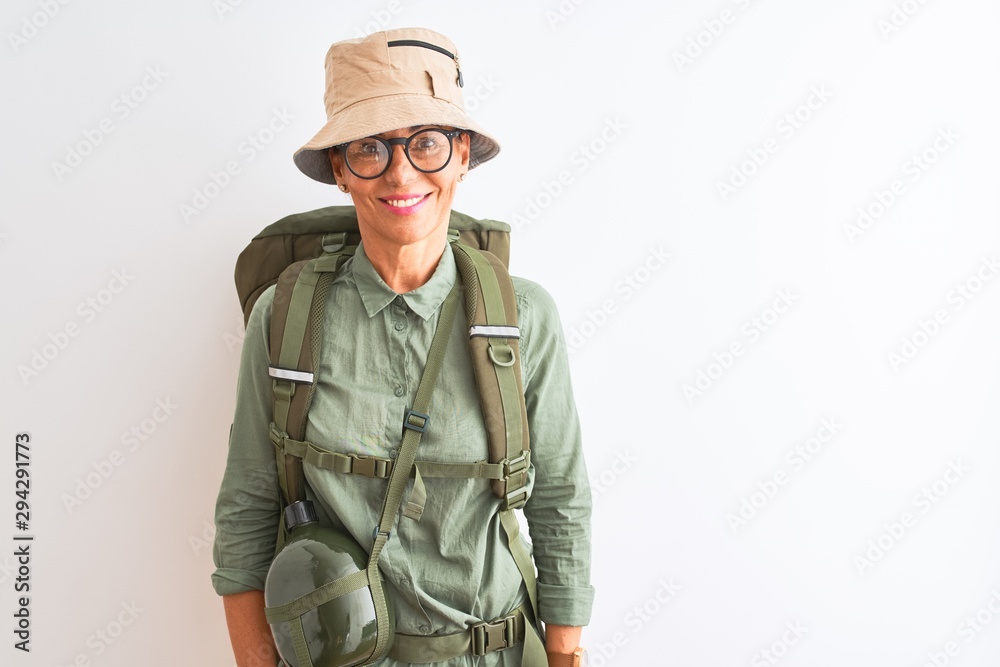Middle age hiker woman wearing backpack canteen hat glasses over isolated white background with a happy and cool smile on face. Lucky person. Middle age hiker woman wearing backpack canteen hat glasses over isolated white background with a happy and cool smile on face. Lucky person.