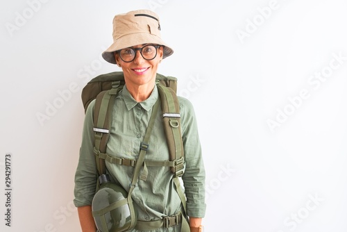 Middle age hiker woman wearing backpack canteen hat glasses over isolated white background with a happy and cool smile on face. Lucky person.