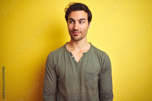 Young handsome man wearing casual t-shirt standing over isolated yellow background smiling looking to the side and staring away thinking.