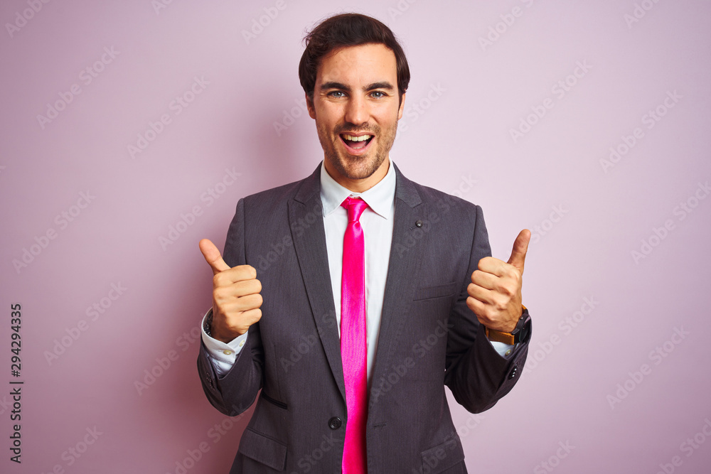 Young handsome businessman wearing suit and tie standing over isolated pink background success sign doing positive gesture with hand, thumbs up smiling and happy. Cheerful expression Young handsome businessman wearing suit and tie standing over isolated pink background success sign doing positive gesture with hand, thumbs up smiling and happy. Cheerful expression