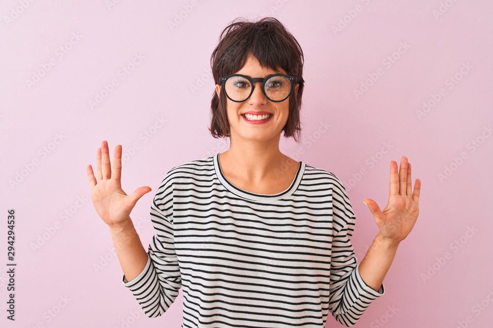 Young beautiful woman wearing striped t-shirt and glasses over isolated pink background showing and pointing up with fingers number ten while smiling confident and happy. Young beautiful woman wearing striped t-shirt and glasses over isolated pink background showing and pointing up with fingers number ten while smiling confident and happy.