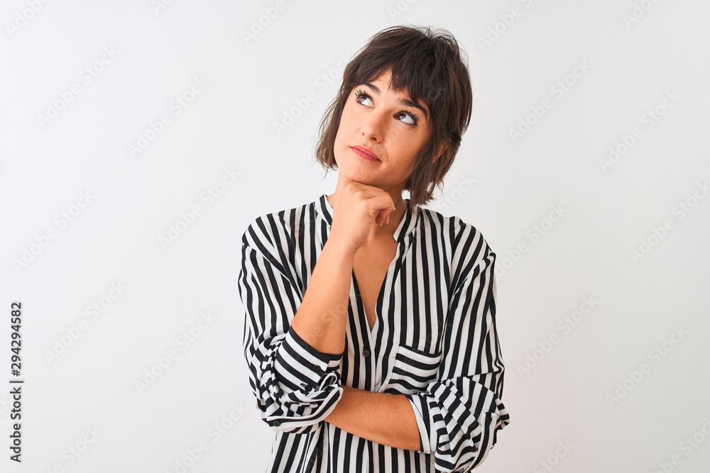 Young beautiful woman wearing striped shirt standing over isolated white background with hand on chin thinking about question, pensive expression. Smiling with thoughtful face. Doubt concept. Young beautiful woman wearing striped shirt standing over isolated white background with hand on chin thinking about question, pensive expression. Smiling with thoughtful face. Doubt concept.