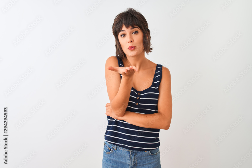 Young beautiful woman wearing striped t-shirt standing over isolated white background looking at the camera blowing a kiss with hand on air being lovely and sexy. Love expression. Young beautiful woman wearing striped t-shirt standing over isolated white background looking at the camera blowing a kiss with hand on air being lovely and sexy. Love expression.