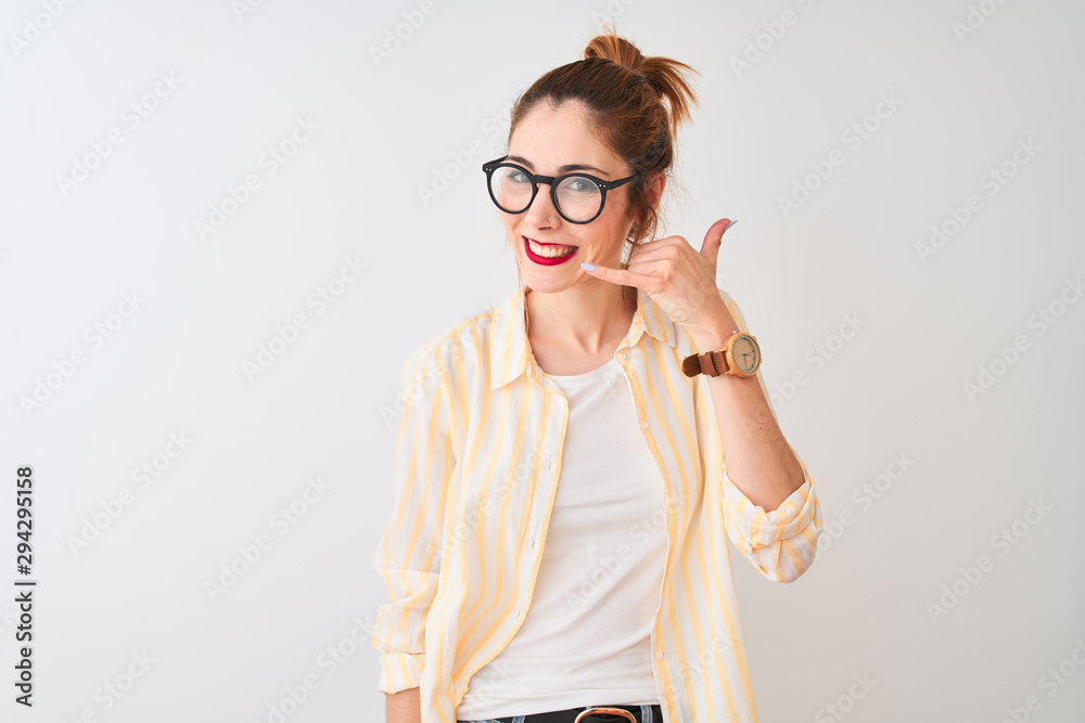 Redhead woman wearing striped shirt and glasses standing over isolated white background smiling doing phone gesture with hand and fingers like talking on the telephone. Communicating concepts.