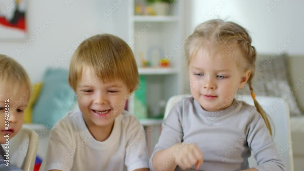 Happy little boys and girl slapping toy tower and smiling as it crushing down on table while playing together in kindergarten Happy little boys and girl slapping toy tower and smiling as it crushing down on table while playing together in kindergarten