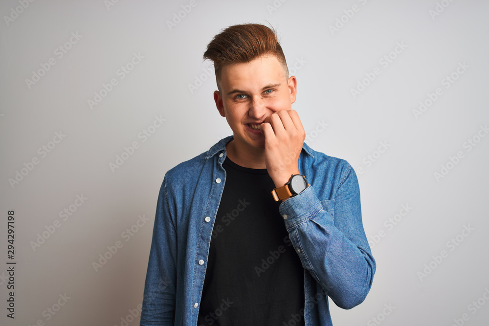 Young handsome man wearing denim shirt standing over isolated white background looking stressed and nervous with hands on mouth biting nails. Anxiety problem. Young handsome man wearing denim shirt standing over isolated white background looking stressed and nervous with hands on mouth biting nails. Anxiety problem.