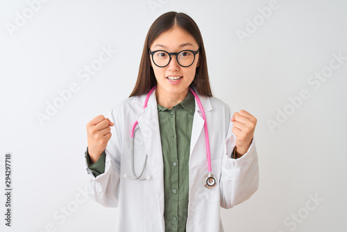 Young chinese dooctor woman wearing glasses stethoscope over isolated white background celebrating surprised and amazed for success with arms raised and open eyes. Winner concept.