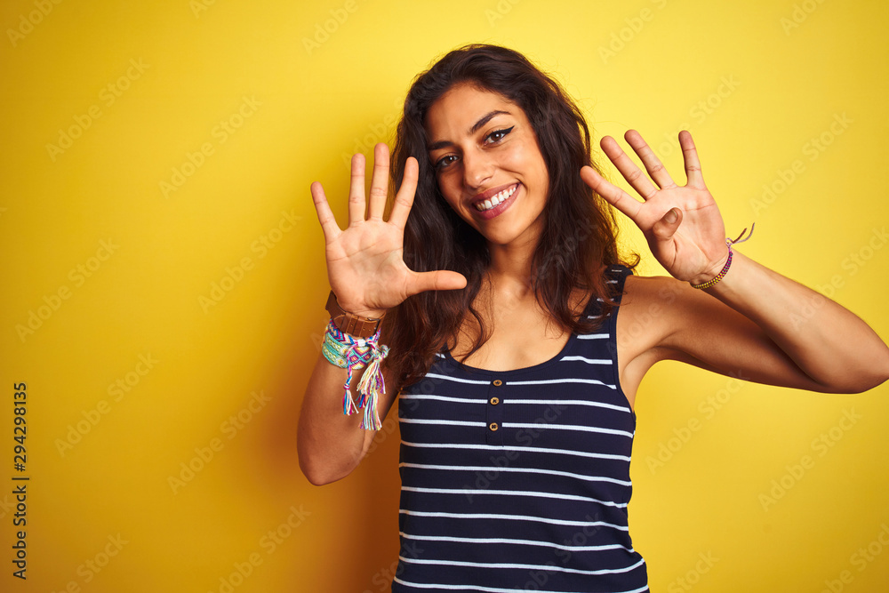 Young beautiful woman wearing striped t-shirt standing over isolated yellow background showing and pointing up with fingers number nine while smiling confident and happy. Young beautiful woman wearing striped t-shirt standing over isolated yellow background showing and pointing up with fingers number nine while smiling confident and happy.