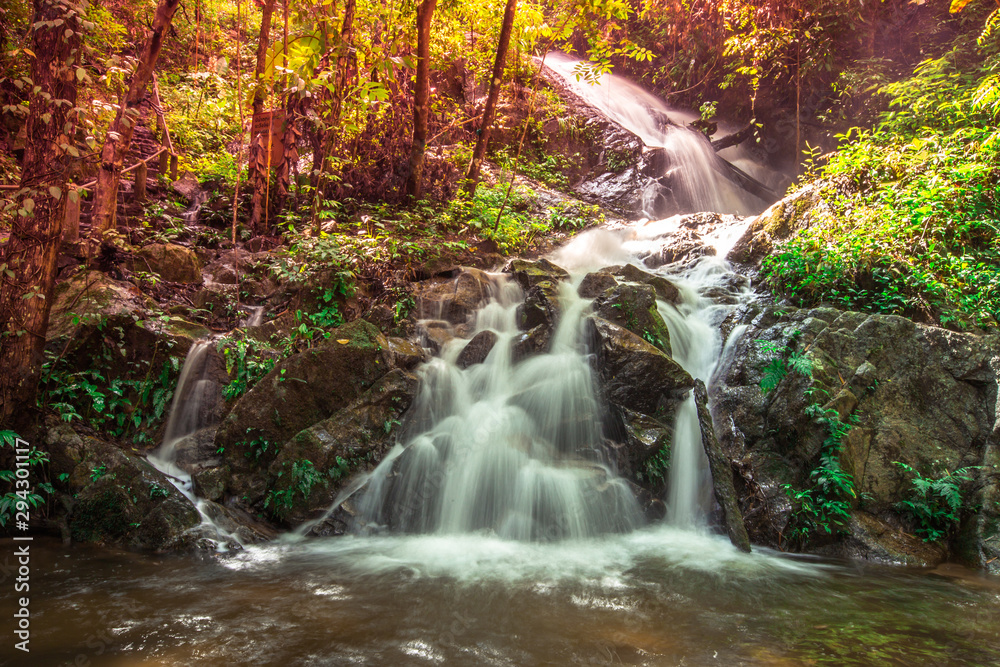 Natural blurred background of waterfalls, fast-flowing currents and water droplets from the wind blowing among the rocks and surrounded by big trees, spontaneous beauty Natural blurred background of waterfalls, fast-flowing currents and water droplets from the wind blowing among the rocks and surrounded by big trees, spontaneous beauty