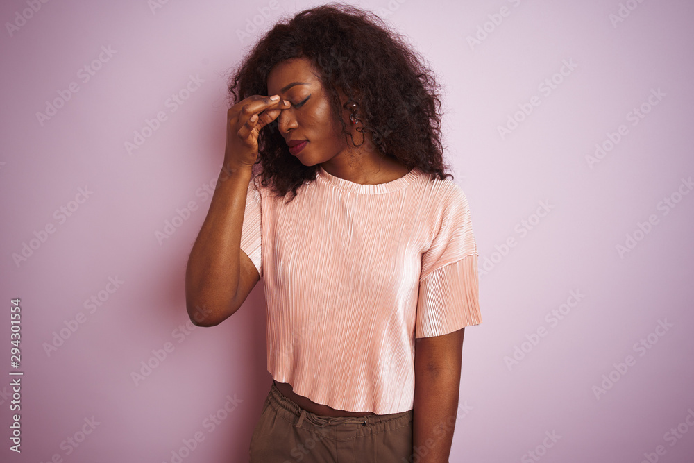 Young african american woman wearing t-shirt standing over isolated pink background tired rubbing nose and eyes feeling fatigue and headache. Stress and frustration concept. Young african american woman wearing t-shirt standing over isolated pink background tired rubbing nose and eyes feeling fatigue and headache. Stress and frustration concept.