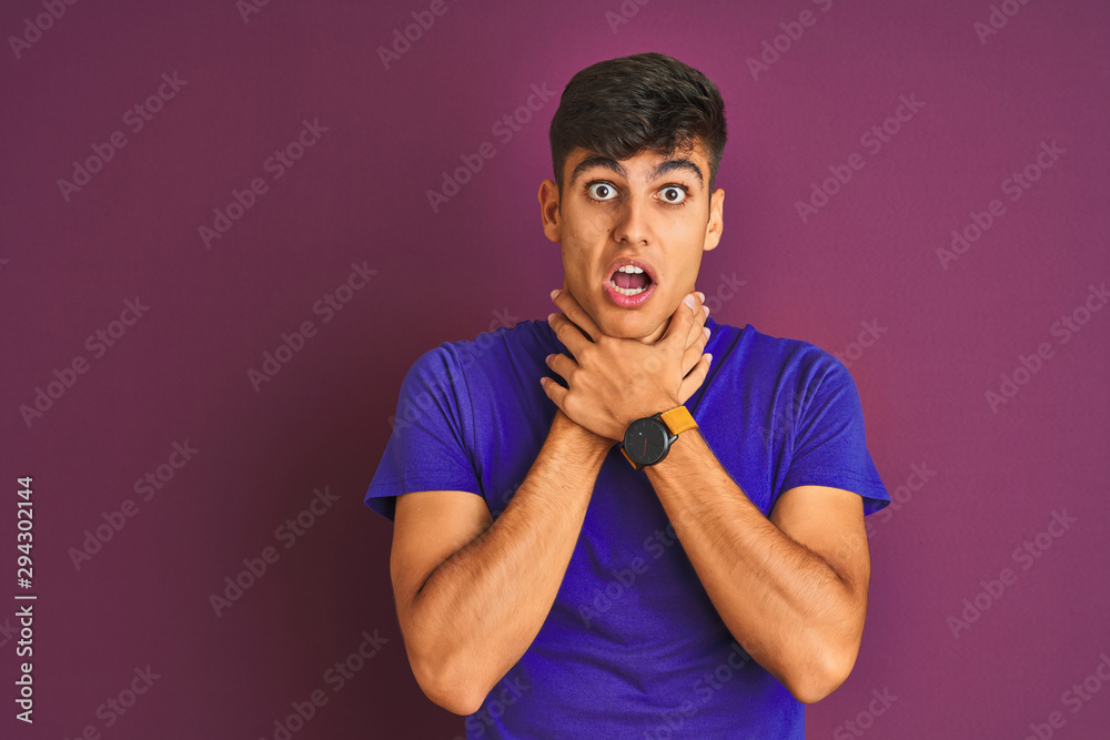 Young indian man wearing t-shirt standing over isolated purple background shouting and suffocate because painful strangle. Health problem. Asphyxiate and suicide concept. Young indian man wearing t-shirt standing over isolated purple background shouting and suffocate because painful strangle. Health problem. Asphyxiate and suicide concept.