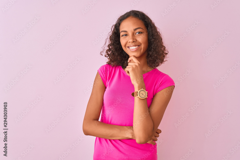 Young brazilian woman wearing t-shirt standing over isolated pink background looking confident at the camera smiling with crossed arms and hand raised on chin. Thinking positive. Young brazilian woman wearing t-shirt standing over isolated pink background looking confident at the camera smiling with crossed arms and hand raised on chin. Thinking positive.