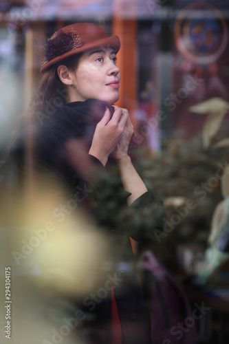 retro portrait of woman through the cafe window in hat and coat close up photo