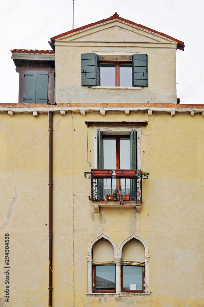 Yellow wall of an old house with windows and a balcony in Venetian style