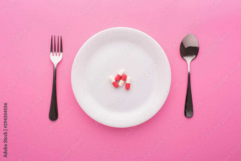 Fototapeta Suplement diety na talerzu z widelcem i łyżką na różowym tle