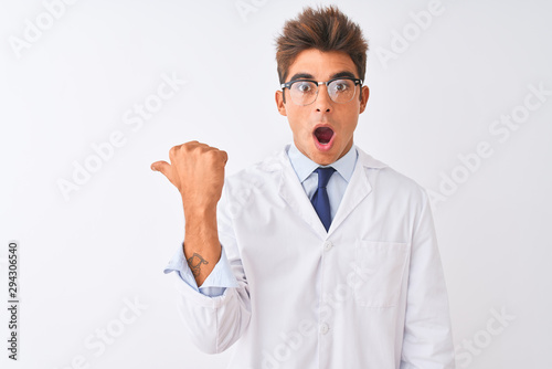 Young handsome sciencist man wearing glasses and coat over isolated white background Surprised pointing with hand finger to the side  open mouth amazed expression.